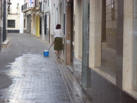 Una vecina de la calle Antonio de la Barrera, limpiando su puerta después de una noche de botellón.